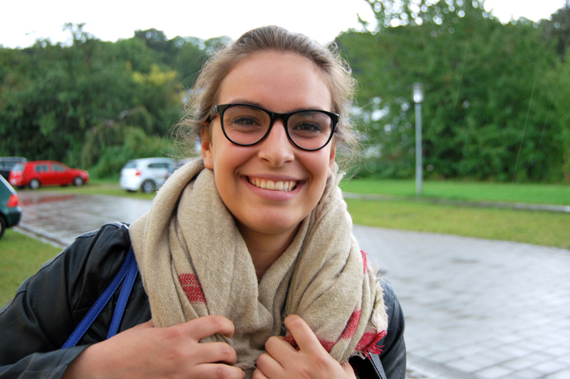 Eine Frau mit schwarzer Brille und Schal lächelt motiviert in die Kamera.