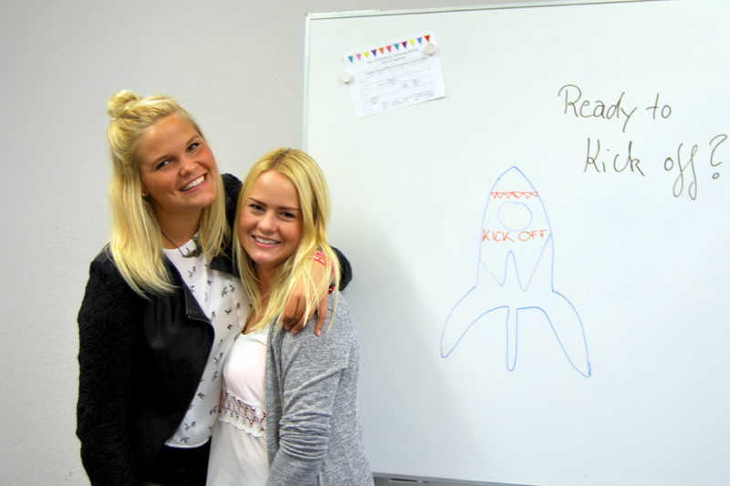 Zwei Frauen stehen Schulter an Schulter neben einem Whiteboard, auf dem eine Rakete zu sehen ist.