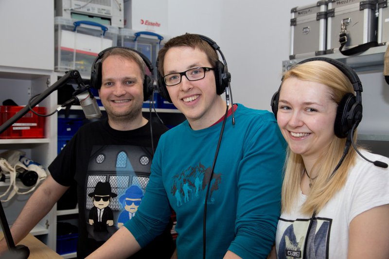 Zwei Männer und eine Frau stehen im Studio des CampusRadioAktiv und lächeln freundlich in die Kamera.