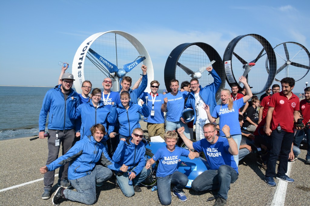 Ein Team junger Sportler:innen in blauen Monturen, steht stolz neben ihren Gegenwindrädern.