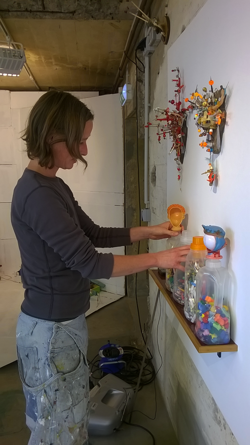 Eine Frau stellt, mit bunten Spielsteinen gefüllte, Waschmittelgefäße auf einem Regal auf.