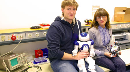 Ein Student und eine Studentin, sitzen mit ihren Robotern in einem Labor.