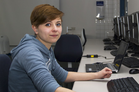 Eine Frau mit kurzen Haaren, sitzt in einem Computerlabor.