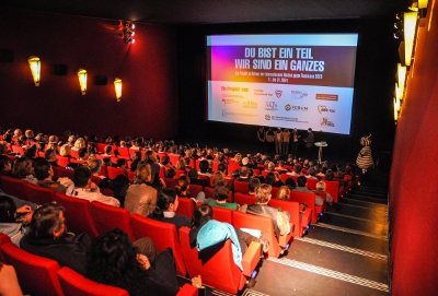 Ein Kinosaal, mit rotenr Bestuhlung, ist bis auf den letzten Platz belegt.