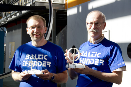 Zwei ältere Männer, in blauem "Baltic Thunder" T-Shirt, lächeln zufrieden in die Kamera.