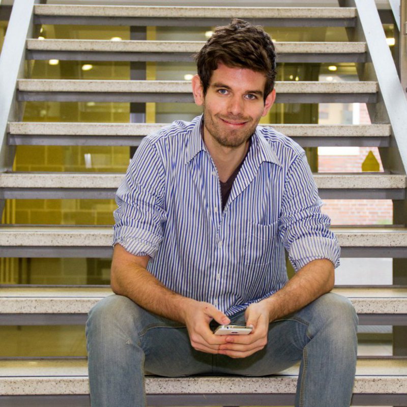 Ein Mann in blau-gestreiftem Hemd sitzt auf einer Treppe und lächelt freundlich in die Kamera.