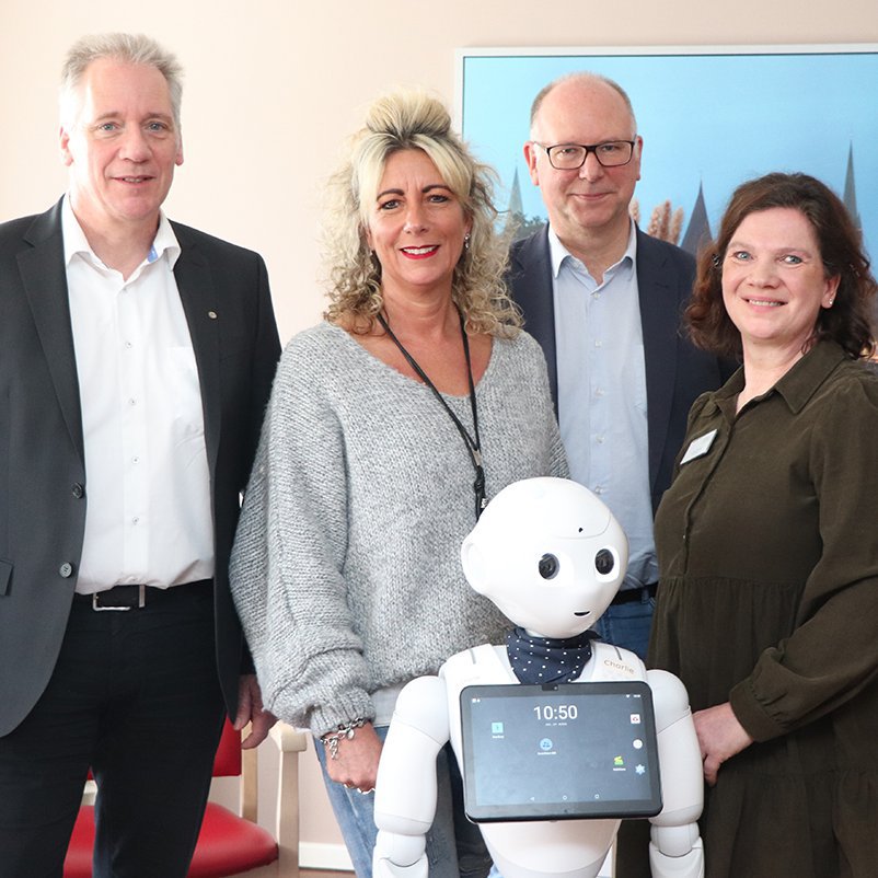 Zwei Männer und zwei Frauen stehen nebeneinander, vor íhnen steht ein kleiner humanoider Roboter. (v.l.): Jörg Brekeller vom VdEK, Doreen Boniakowsky von der Diakonie NNO , Prof. Lüssem von der FH Kiel sowie Jutta Tandler vom Pflegezentrum Travetal.
