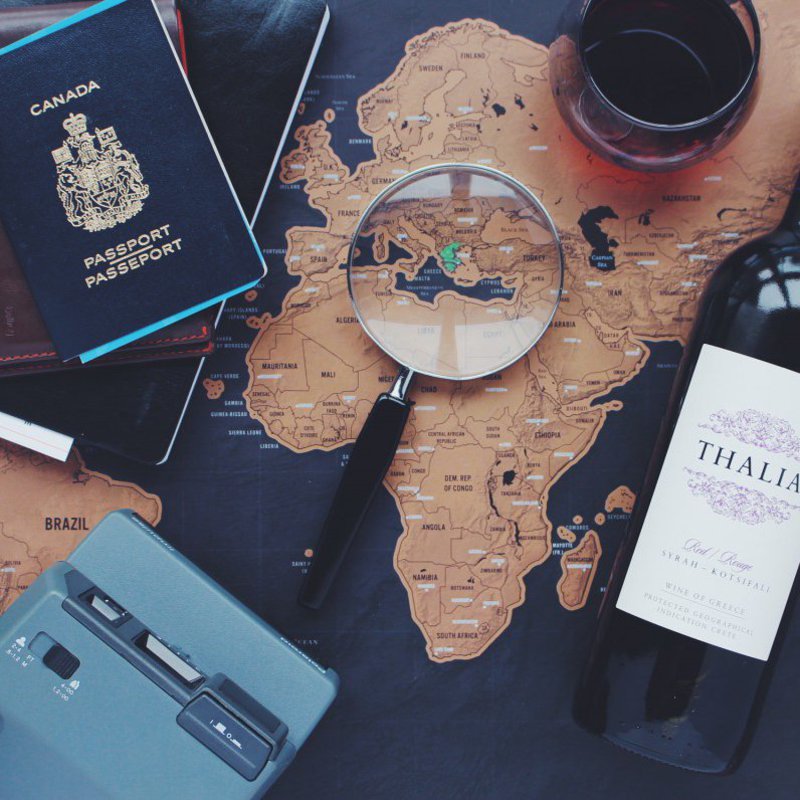 Auf einer Landkarte liegt eine Lupe, eine Flasche Wein und Reisedokumente.