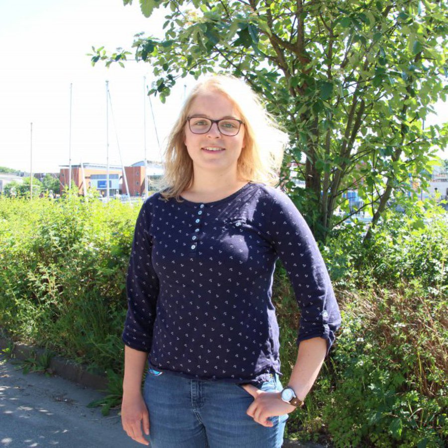 Eine Frau posiert auf einem Parkplatz und schaut freundlich in die Kamera.