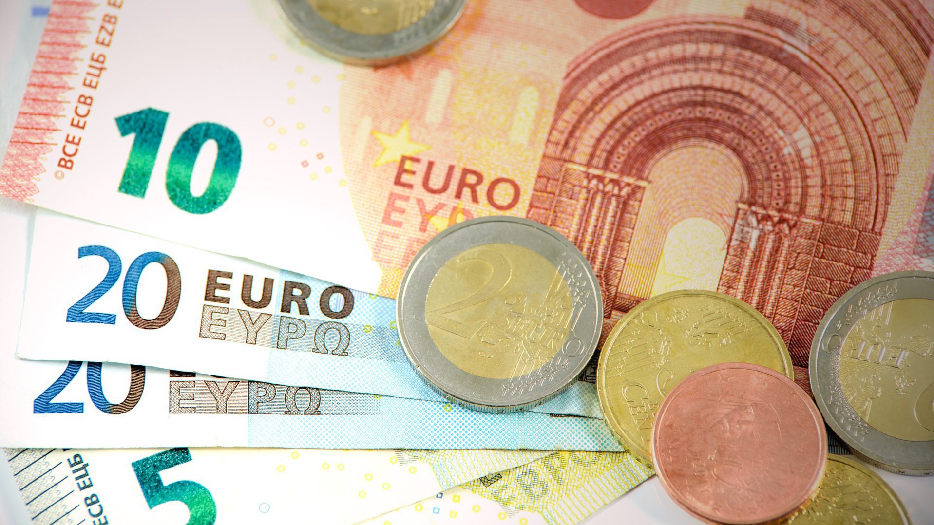 Geldscheine liegen aufgefächert auf einer Fläche und zwei Euro-Münzen liegen drauf verteilt.