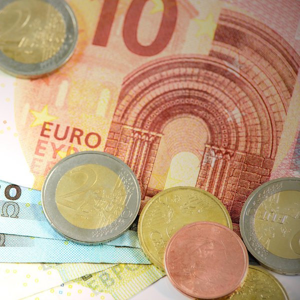 Geldscheine liegen aufgefächert auf einer Fläche und zwei Euro-Münzen liegen drauf verteilt.
