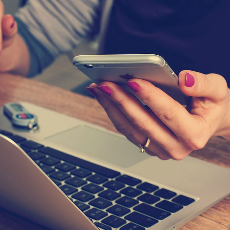 Frau vor dem Laptop und mit Handy in der Hand