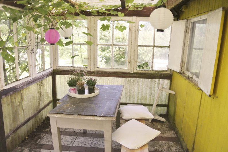 Ein verglaster Vorraum zu einer Gartenlaube ist von innen und außen bewachsen.