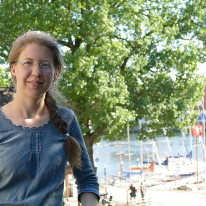 Eine Frau posiert auf einer Anhöhe, im Hintergrund ist unten ein Yachthafen zu sehen.