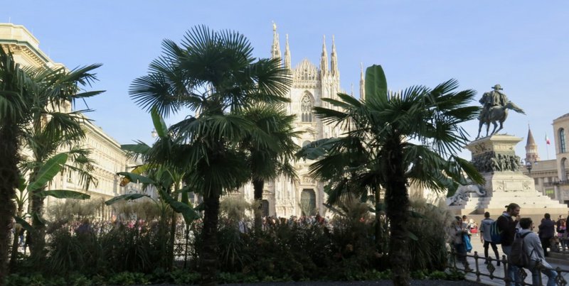 Palmen und Gebüsche erschweren die Sicht auf eine große Sandstein Kathedrale.