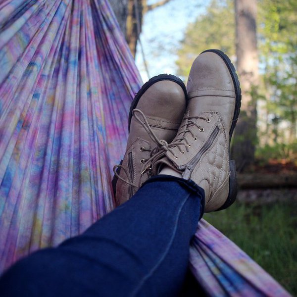 Zwei mit Stiefeln bekleidete Füße liegen in einer lilanen Hängematte im Freien.
