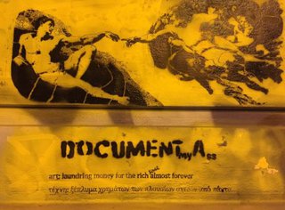 Ein gelbes Plakat, auf dem sich die Fingerspitzen von zwei Engeln berühren. Es trägt die Aufschrift " Documenta".