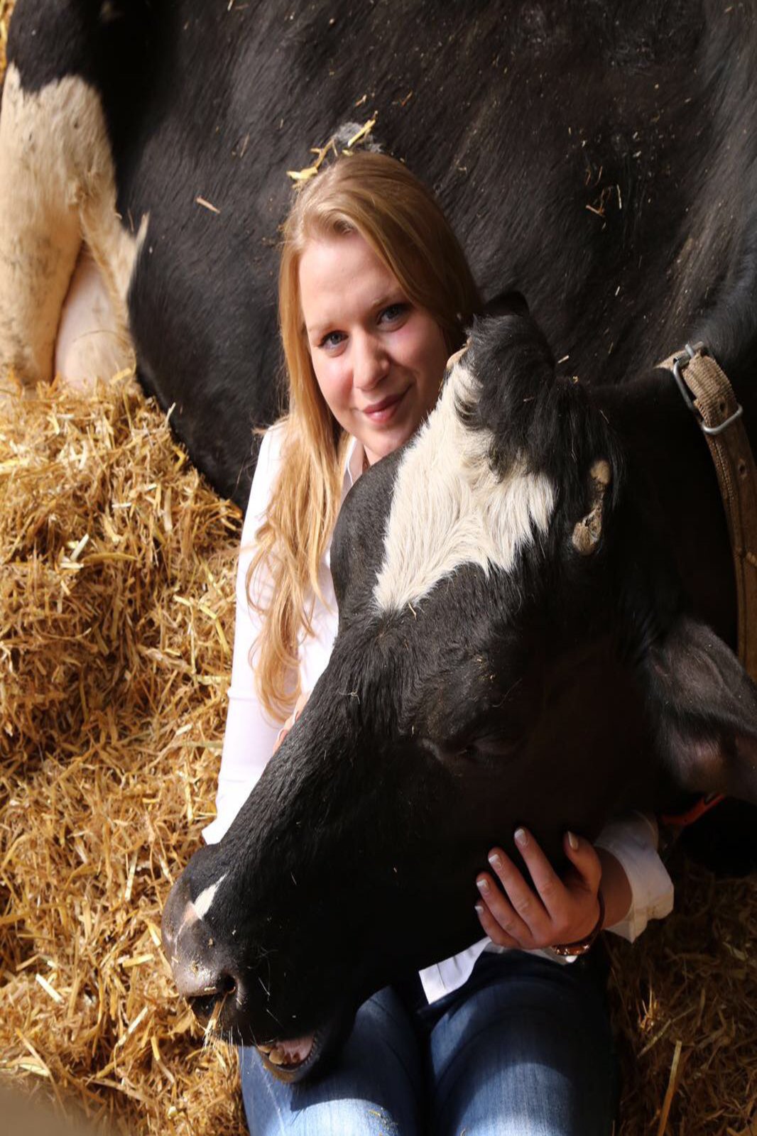 Nina Zingelmann angeschmiegt an eine Kuh, die im Stroh liegt.