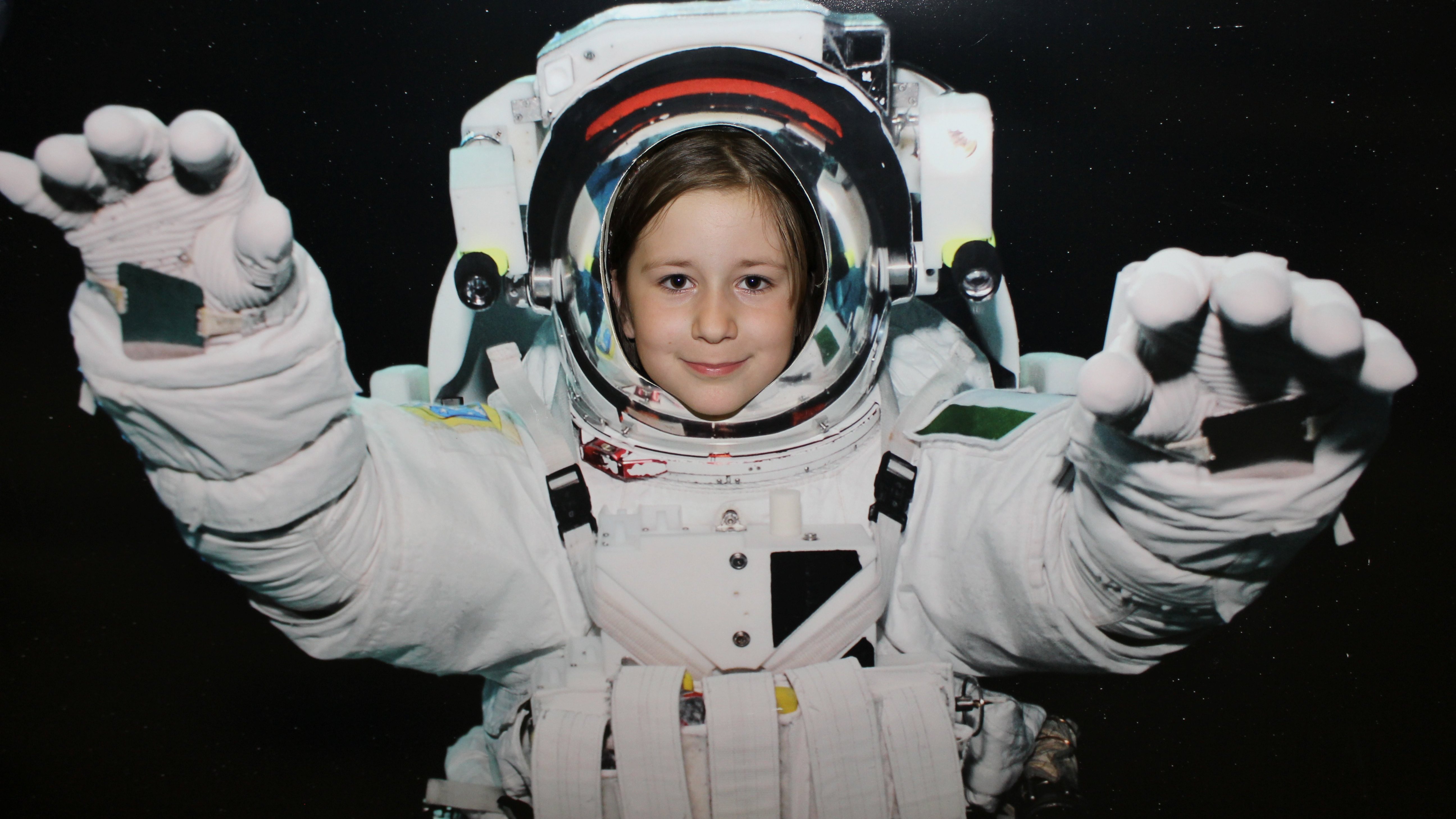 Mädchen guckt durch eine Fotowand, die sie als Astronautin zeigt