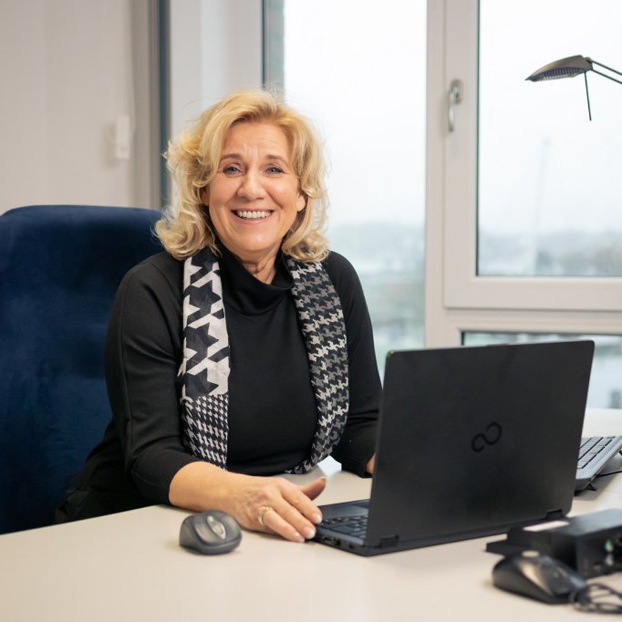 Marion Mayr-Tschofenig sitzt an einem Schreibtisch und lächelt in die Kamera.