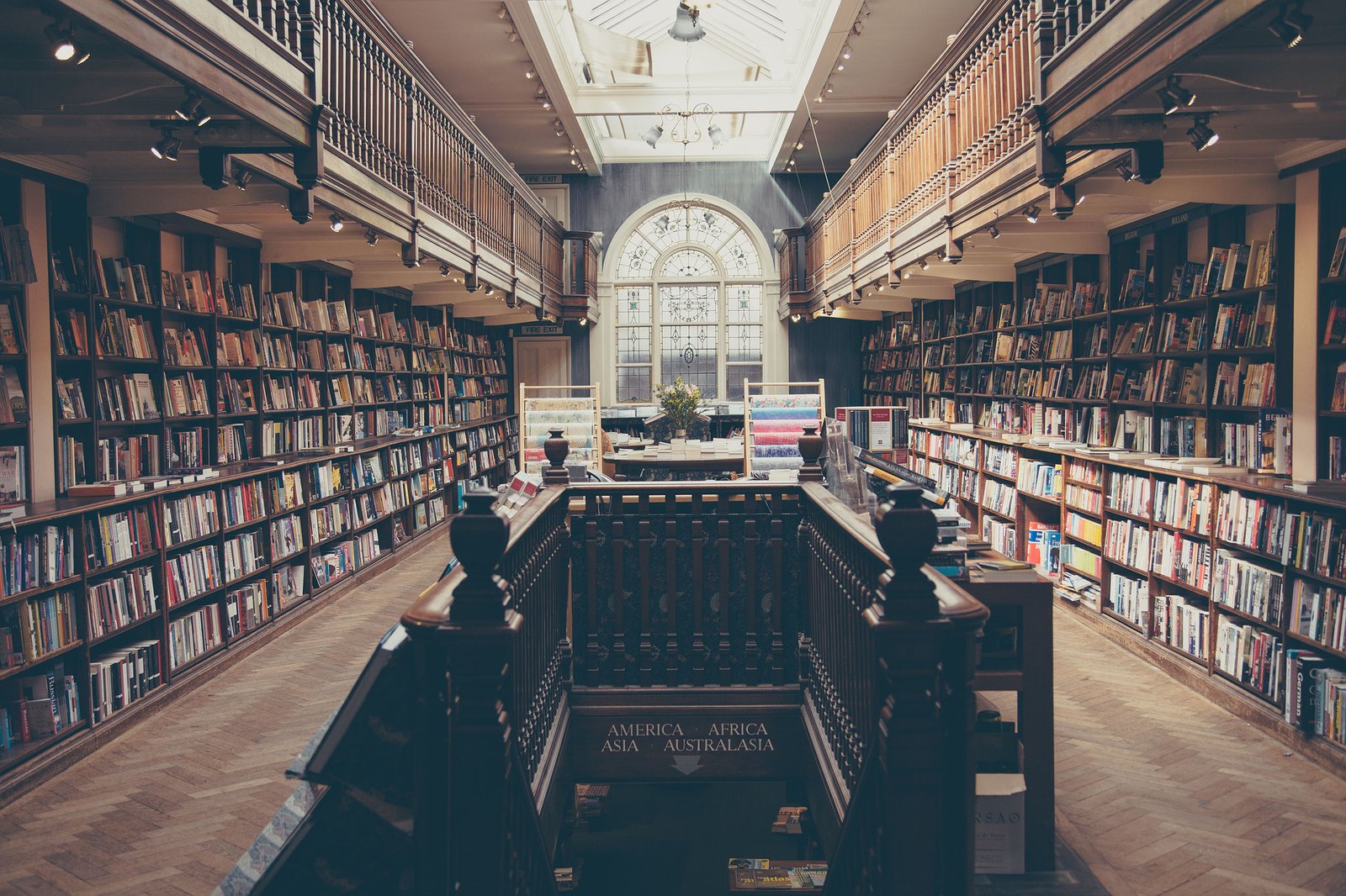 Ein schöner hölzerner Flur in einer alt anmutenden Bibliothek. Es führt eine Treppe nach unten und der Raum ist in disiges Licht geatucht.