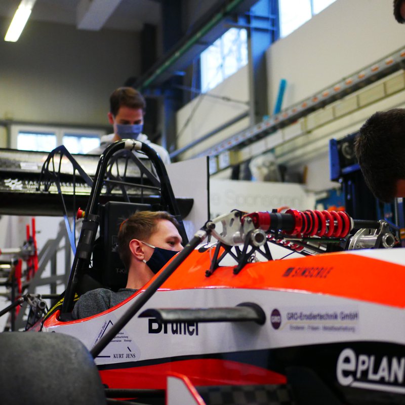 Ein Student, der eine Maske trägt, sitzt in einem Rennwagen von Raceyard.