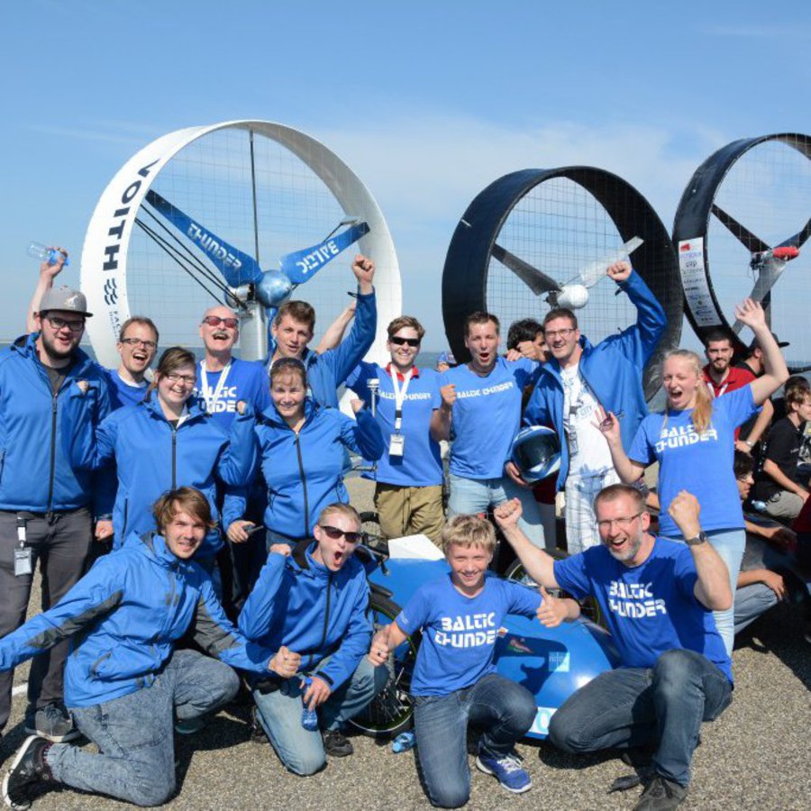 Ein Team junger Sportler:innen in blauen Monturen, steht stolz neben ihren Gegenwindrädern.