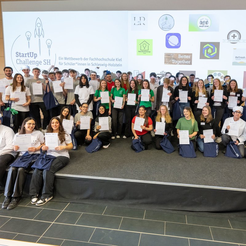 auf der Bühne des Audimax der FH Kiel stehen viele Schülerinnen und Schüler. Sie haben an dem Finale der StartUp Challenge 2023 teilgenommen