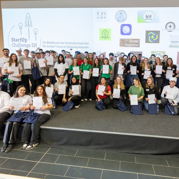 auf der Bühne des Audimax der FH Kiel stehen viele Schülerinnen und Schüler. Sie haben an dem Finale der StartUp Challenge 2023 teilgenommen