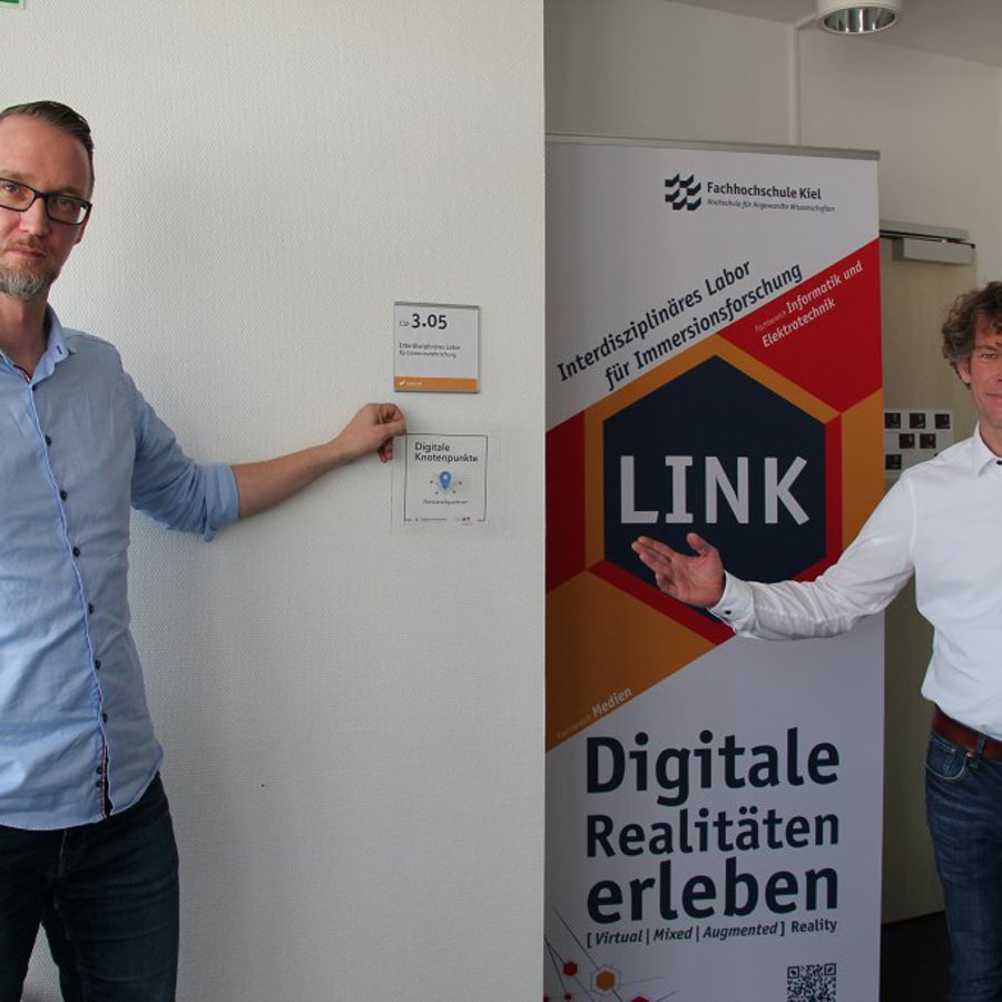 Prof. Patrick Rupert-Kruse (links) hält die Plakette mit der Aufschrift Digitaler Knotenpunkt in der Hand, Prof. Felix Woehlk sthe rechts neben ihm.