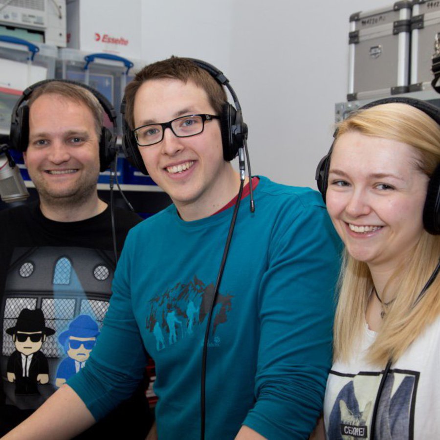 Zwei Männer und eine Frau stehen im Studio des CampusRadioAktiv und lächeln freundlich in die Kamera.