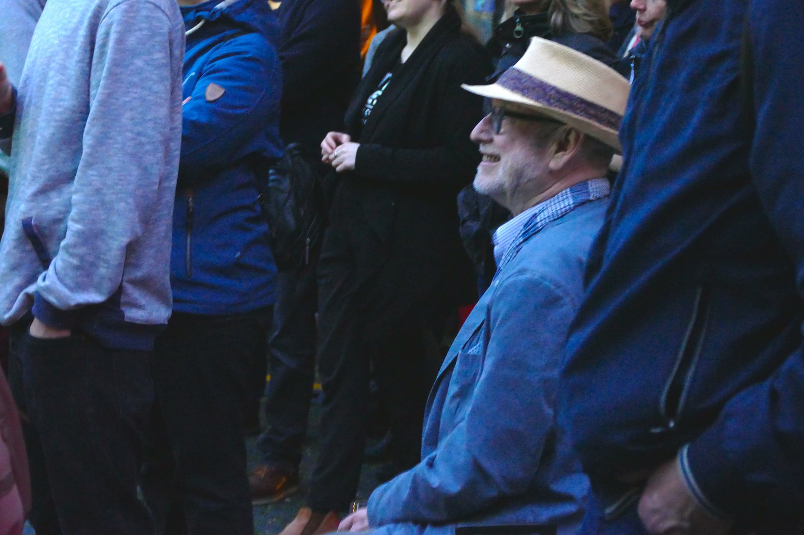 Ein Mann sitzt inmitten einer stehenden Menschenmenge.