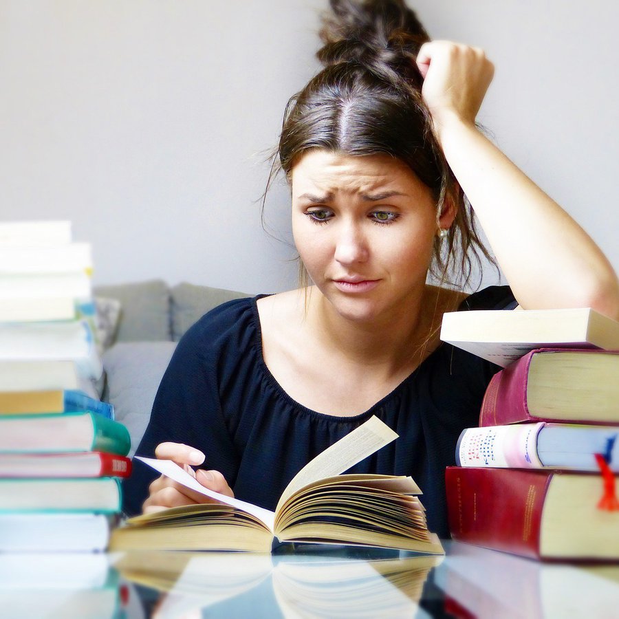 Frau guckt skeptisch in ein Buch, vor ihr hohe Bücherstapel