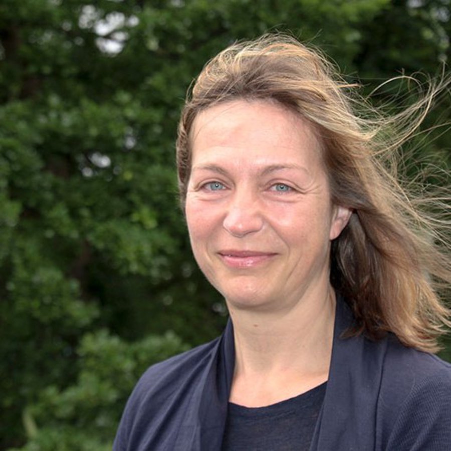 Einer Frau weht der Wind durch ihre Haare, während sie in die Kamera lächelt.