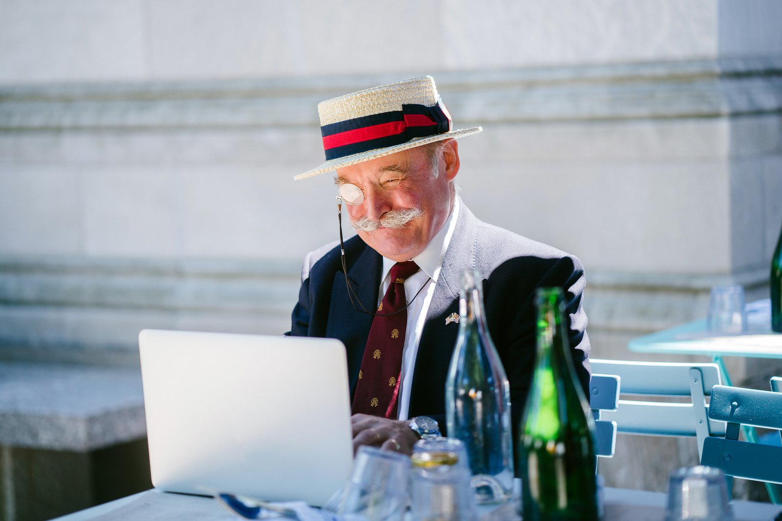 Ein sehr gut gekleideter älterer Mann sitz draussen im Halbschatten an seinem Laptop.