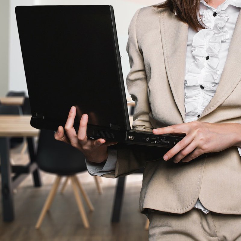 Frau im Anzug mit Laptop auf dem Arm