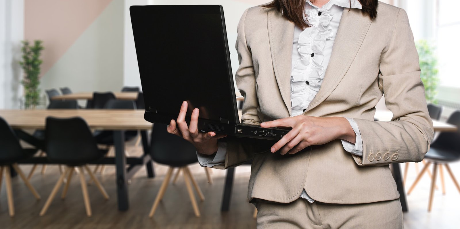 Eine Frau im Anzug steht in einem Konferenzraum und hält einen Laptop in den Händen.