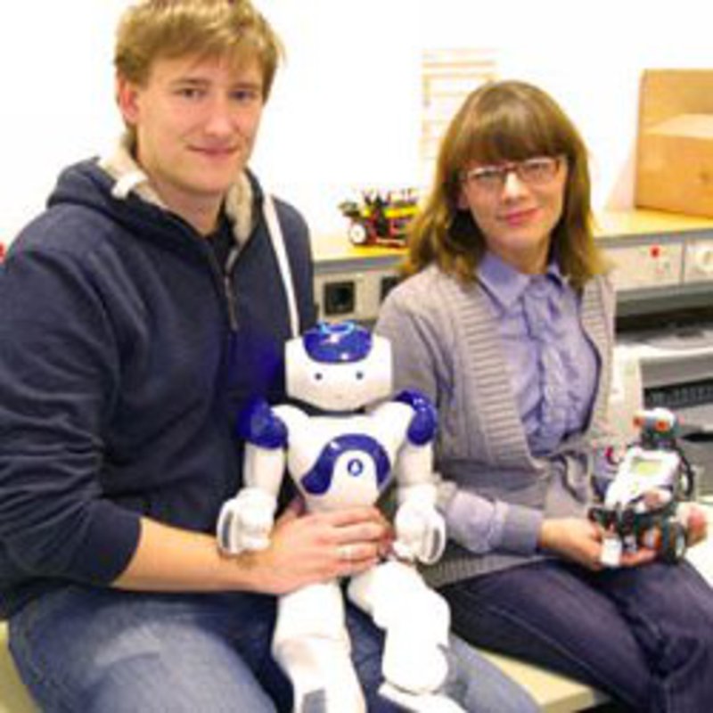 Ein Student und eine Studentin, sitzen mit ihren Robotern in einem Labor.