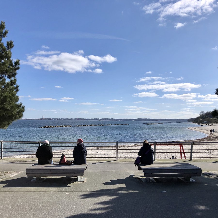 Strandpromenade mit Bänken und sitzenden Menschen