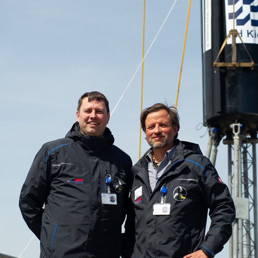 Prof. Christian Keindorf und Andreas Glaß stehen vor dmeWellenkraftwerk, das am Kran hängt.  