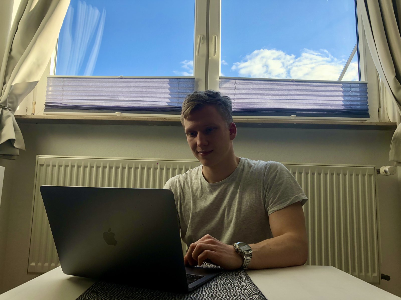Ein Student sitzt vor seinem Laptop. Im Hintergrund kann man durch ein Fenster den Himmel sehen.