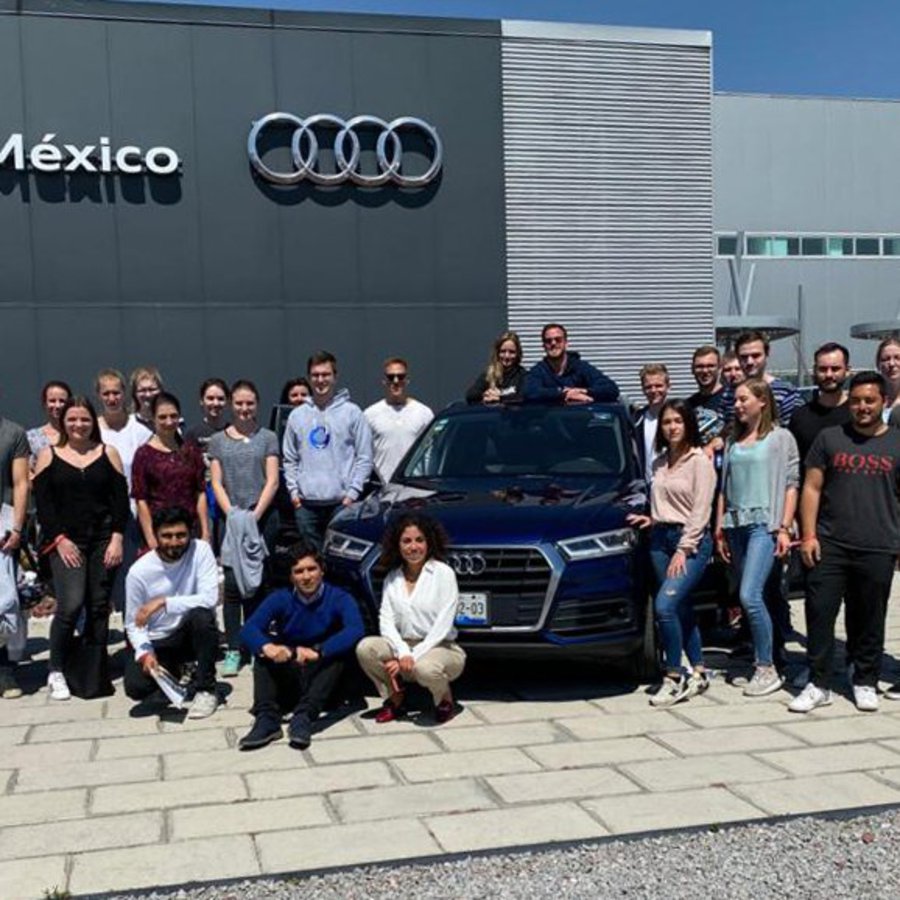 Eine große, gemischte Gruppe von Personen posiert vor einem Audi Autohaus.