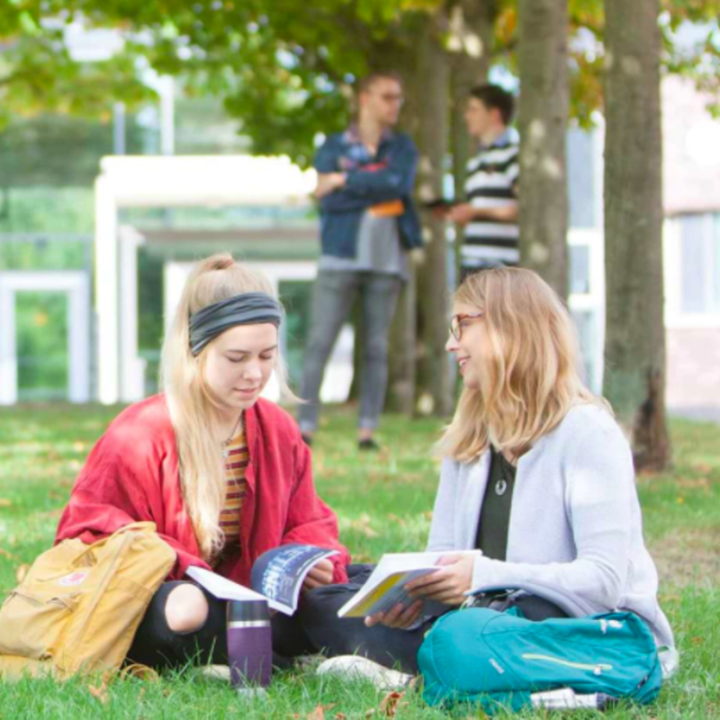 Zwei Studentinnen sitzen auf einer Wiese, daneben in Textform: FIT für die Zukunft.