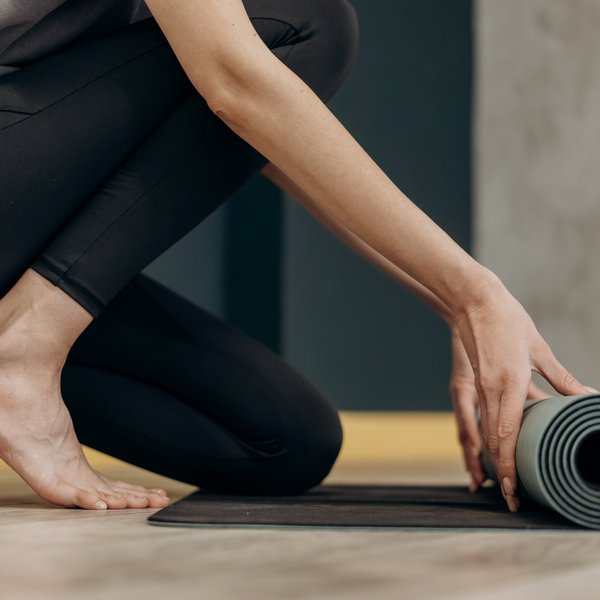 Eine Frau kniet halb auf dem Boden und rollt eine Yogamatte aus