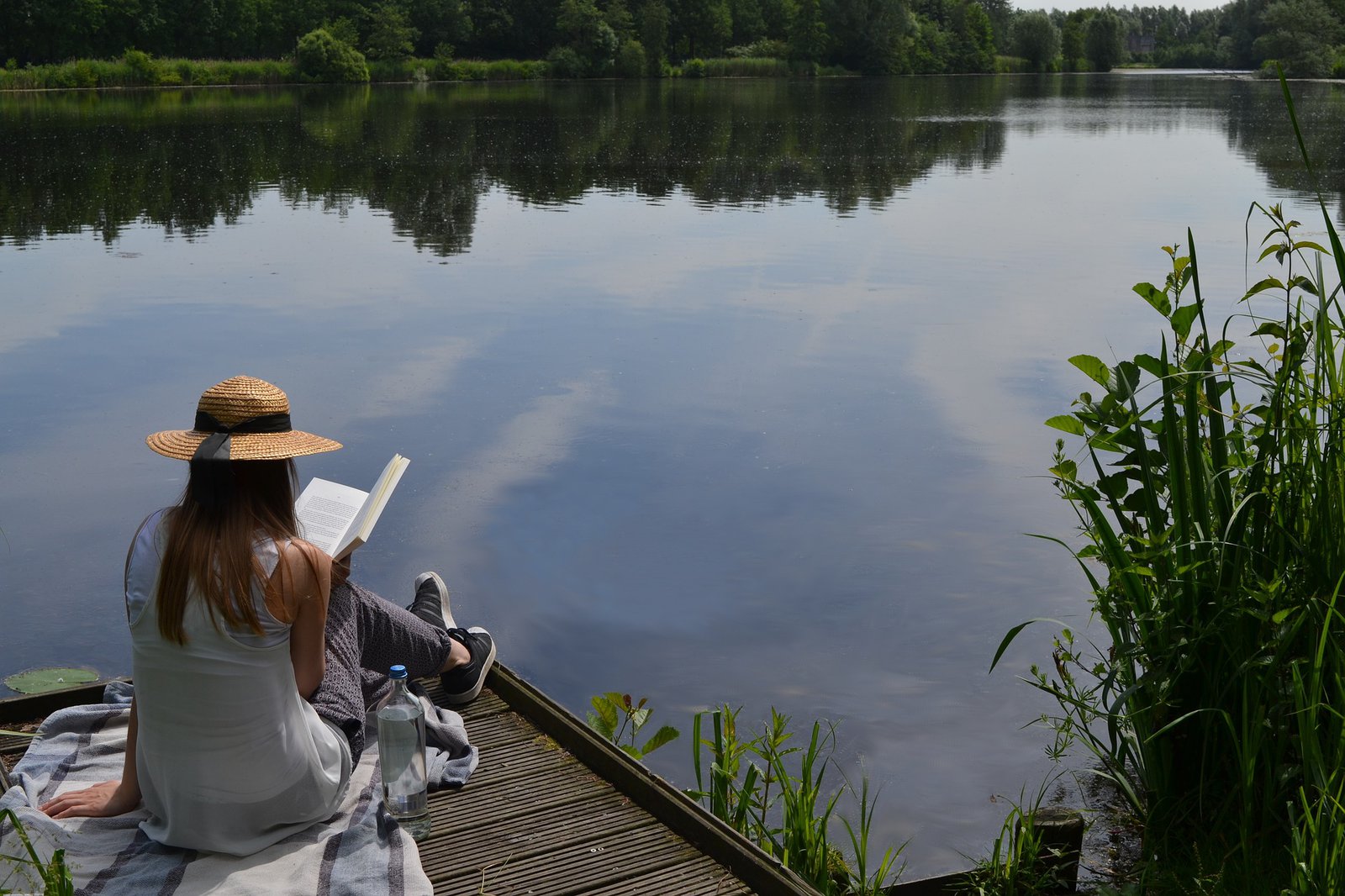 Eine Frau sitzt an einem See und liest ein Buch.