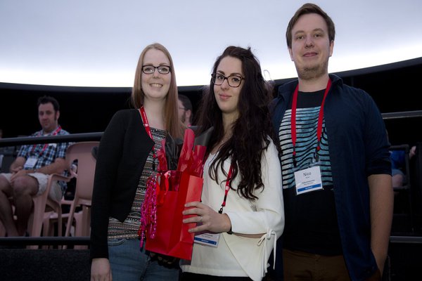 drei Studierende posieren und halten eine Geschenktüte in den Händen.