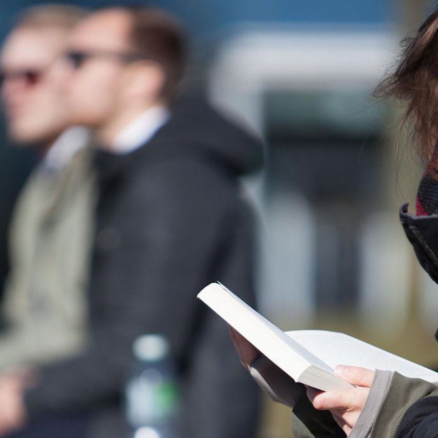 Frau liest im Buch, unscharf im Hintergrund zwei Menschen