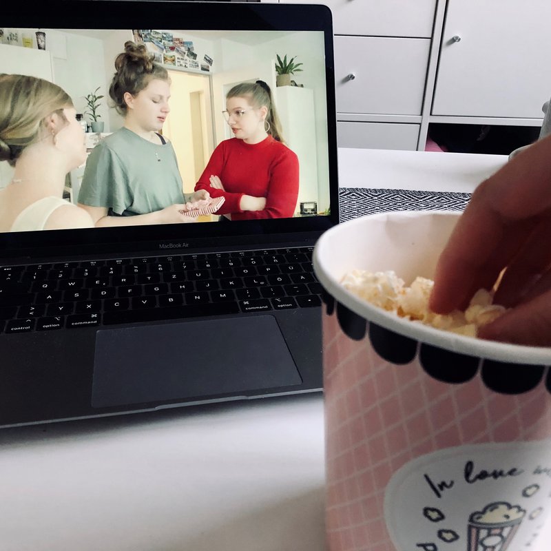 Laptop, Becher Popcorn und Hand