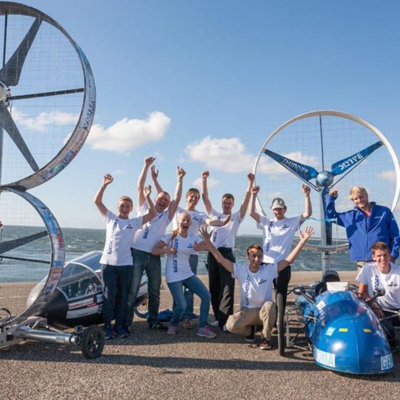 Ein Team von Propellerrennwagenfahrern steht jubelnd neben ihren beiden Fahrzeugen.