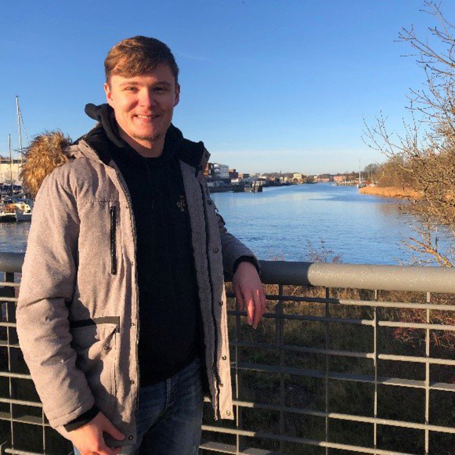 Der Bachelorstudent Michael Siegert steht auf einer Brücke und lächelt in die Kamera.